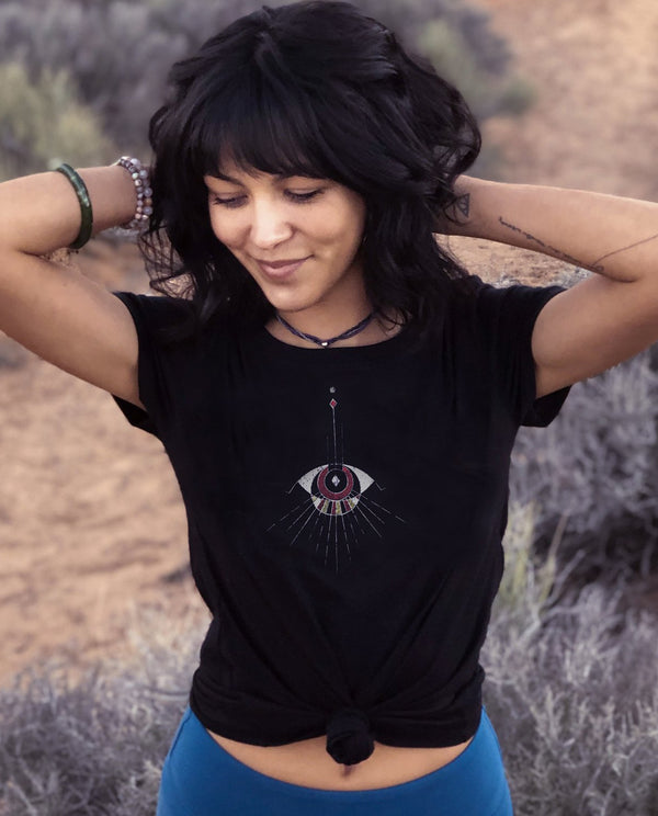 Woman wearing unisex black T, styled and knotted at stomach. Unique abstract eye design, handdrawn art.