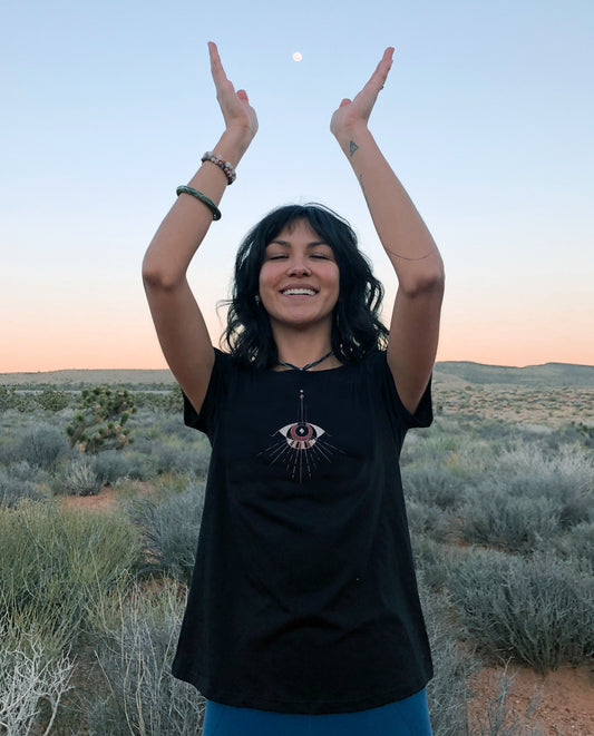 Woman wearing unisex black T, styled and knotted at stomach. Unique abstract eye design, handdrawn art.